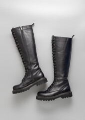 Trendy fashionable black leather knee high lace up women pair boots on grey