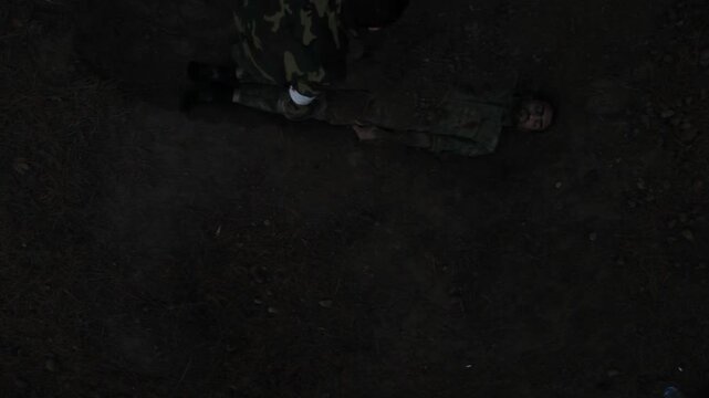 An exhausted soldier in camouflage crawls through dirt in a forest trench. He appears desperate and dirty, struggling to move after burying a fallen comrade during combat operations.

