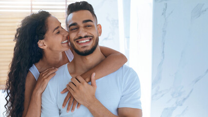 A happy couple enjoys a playful interaction in a stylish room filled with natural light. The woman leans in affectionately while the man smiles broadly, showcasing a close bond.