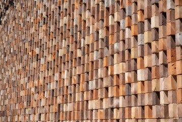 Clay bricks are stacked in a pattern on a wall. Different colors and textures create a strong visual effect. The sunlight highlights the details of the arrangement
