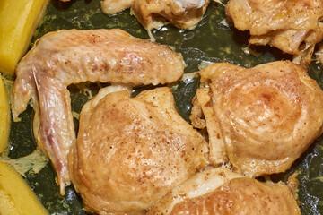 Oven-baked chicken pieces with potato slices and seasoning mixture. Close-up.