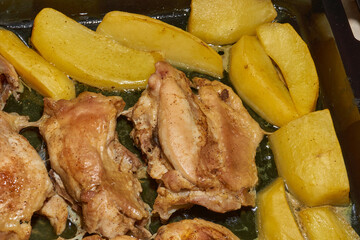 Oven-baked chicken pieces with potato slices and seasoning mixture. Close-up.