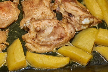 Oven-baked chicken pieces with potato slices and seasoning mixture. Close-up.