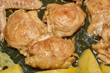 Oven-baked chicken pieces with potato slices and seasoning mixture. Close-up.