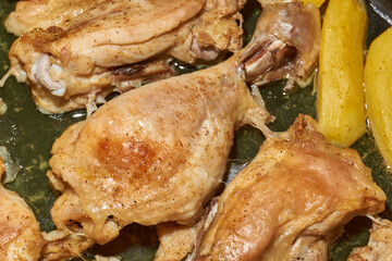 Oven-baked chicken pieces with potato slices and seasoning mixture. Close-up.