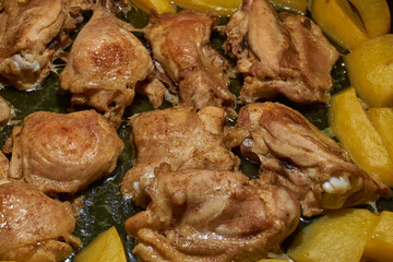 Oven-baked chicken pieces with potato slices and seasoning mixture. Close-up.