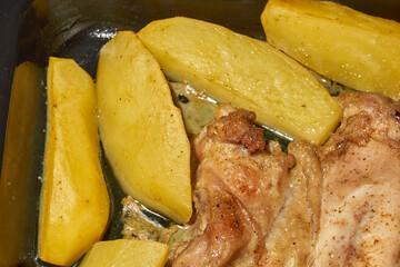 Oven-baked chicken pieces with potato slices and seasoning mixture. Close-up.