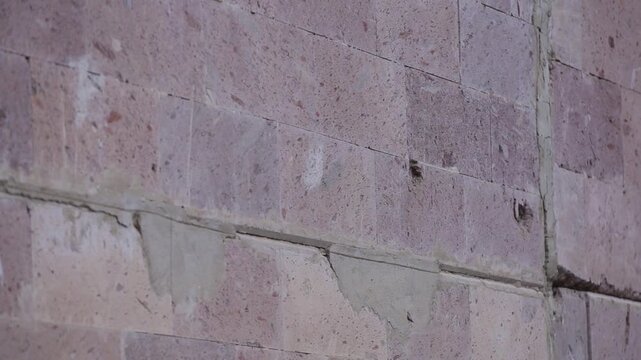 Close up texture of pink stone wall riddled with bullet holes. Angled view showing damaged building facade and window resulting from military conflict or war battle.

