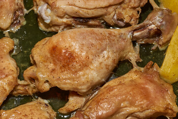 Oven-baked chicken pieces with potato slices and seasoning mixture. Close-up.