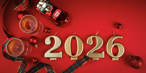 Golden number candles forming 2026 surrounded by red ornaments, ribbon, and glasses on a red background
