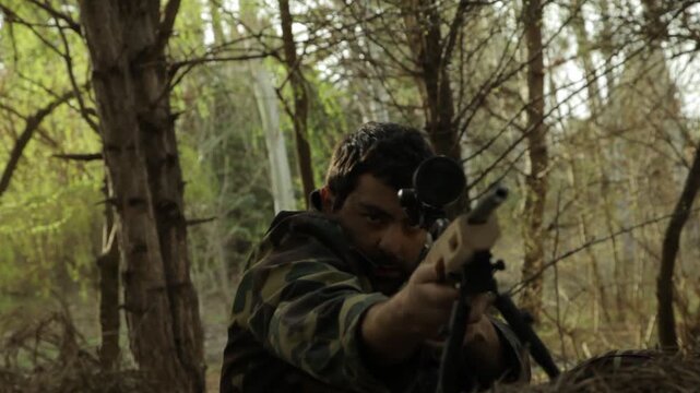 A focused sniper in camouflage uniform lies prone in a dense forest, aiming his rifle with precision while looking through the scope, ready for a crucial mission.