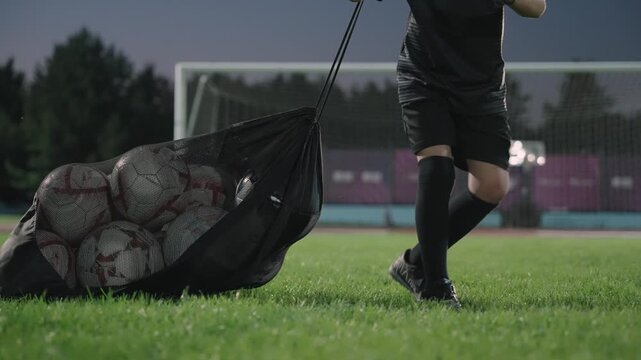 A football boy drags a bag of balls to the stadium at night