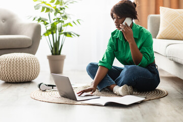 A woman is sitting on the floor in a cozy living room, engaging in a phone conversation while using her laptop. She appears focused on her tasks, surrounded by a serene environment.