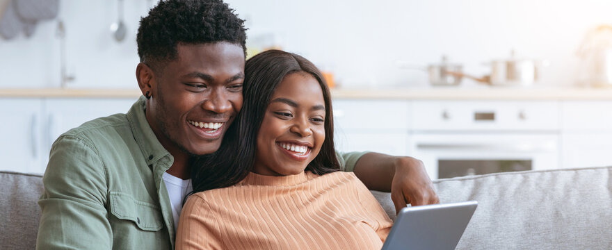 Two friends smile and laugh as they share a moment while looking at a tablet in a modern kitchen. The warm atmosphere and their connection create a joyful scene. - Powered by Adobe