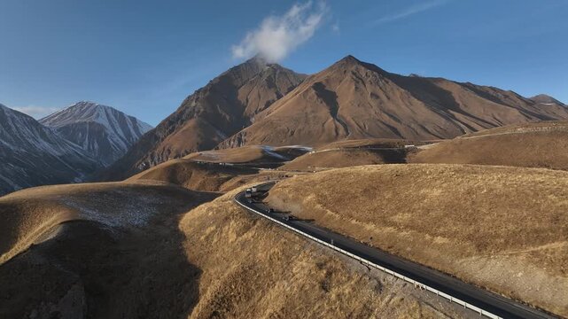 Aerial view of the winding Georgian Military Highway near Gudauri, Georgia. Mountain road surrounded by golden slopes and snowy peaks in early winter.