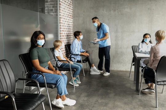 Multiracial people different ages sitting at vaccination site, wearing protective face masks, waiting for immunization against coronavirus while pandemic, doctor having conversation with patients - Powered by Adobe