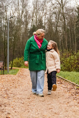 Fototapeta premium Walking mother with daughter on park path. Holding hands shows parenting, care, trust, safety. Outdoor family activity supports bonding, happiness, healthy lifestyle, weekend leisure, forest trail.