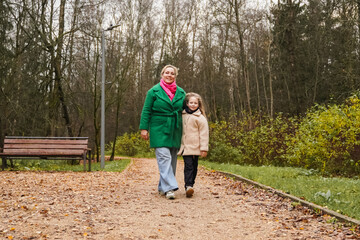 Fototapeta premium Walking mother with daughter on park path. Holding hands shows parenting, care, trust, safety. Outdoor family activity supports bonding, happiness, healthy lifestyle, weekend leisure, forest trail.