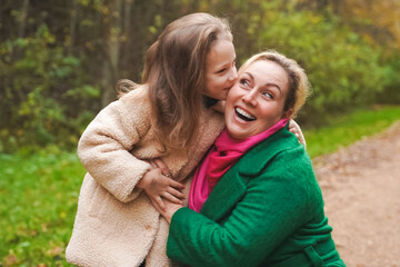 Fototapeta premium Cuddling mother with daughter in park. Smiling family portrait shows love, affection, support. Close bonding supports childhood happiness, motherhood care, trust, safe relationship, outdoor lifestyle.