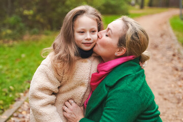 Fototapeta premium Cuddling mother with daughter in park. Smiling family portrait shows love, affection, support. Close bonding supports childhood happiness, motherhood care, trust, safe relationship, outdoor lifestyle.