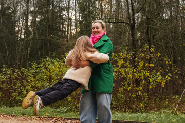 Spinning mother with daughter on park path. Playful hug shows joy, love, active childhood. Outdoor family game supports bonding, trust, balance, motion, energy, healthy lifestyle, weekend fun.