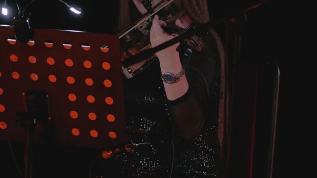 A violinist at work, highlighting the delicate movements of her hands as she plays, against a softly lit background that heightens the mood. Frontal view. Close-up