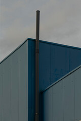 Fototapeta premium Industrial silhouette emerges, Muted sky highlights structured design, Vertical pipelines contrast with subdued sky background, Blue roofing and tall pipe shape define sleek factory appearance