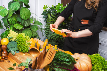Hands photographing pumpkin and fresh vegetables with smartphone on wooden counter in kitchen , capturing ingredients for healthy seasonal meal. Food content, recipe photography and lifestyle concept.