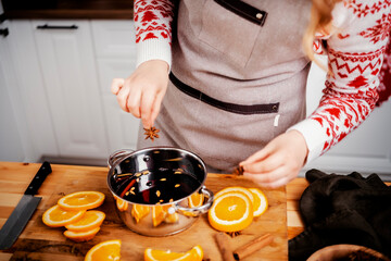 Woman adding star anise and spices to mulled wine in festive Xmas or New Year kitchen preparing...