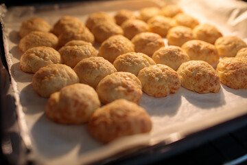 Close-up of golden, freshly baked cheese puffs resting on parchment paper on a baking sheet, illuminated by warm, intense light from above