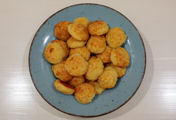 Top-down view of a blue plate heaped with golden, freshly baked cheese puffs  centered on a clean white wooden table surface