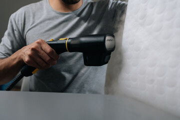 Close-up of unrecognizable using handheld steam cleaner on white foam pillow, sanitizing and disinfecting bedding for improved home hygiene, cleanliness and overall wellbeing. Concept of household.