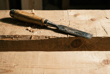 Woodworker's Tool on Timber: A close-up view of a chisel poised on a raw wooden plank, its blade glinting with a touch of light, revealing the artisan's mark.
