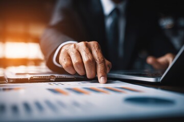 Close-up of a businessman's hand on a glossy laptop, surrounded by strategic documents, with warm lighting highlighting a determined, professional mood