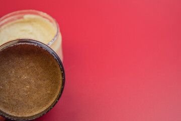 Natural body scrub jar reveals creamy brown texture, set against a vivid red backdrop, highlighting beauty, skincare, and self-care themes in a visually appealing manner