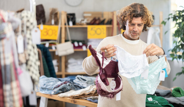 While shopping, man buyer looks at products in store and selects ladys lingerie. Concept of seasonal wardrobe shopping. Client at shopping time leisure activity.