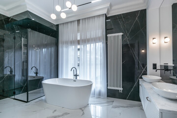 A spacious bathroom with a freestanding bathtub. Large windows let in natural light, highlighting the dark marble walls and elegant modern plumbing.