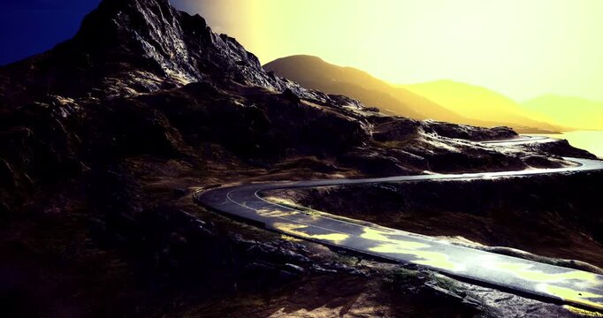 A narrow road meanders along the rocky cliffs, illuminated by a warm golden light. The landscape features dramatic mountains and reflective water in the distance, creating a serene atmosphere.