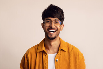 Obraz premium A young man with glasses wears a bright orange jacket over a white shirt, smiling joyfully while facing the camera, showcasing a friendly and approachable demeanor.