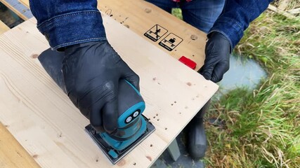 Professional man carpenter using electric sander to polish wood on rough workbench at back yard. Design, carpentry, craftsmanship and handwork concept. High quality 4k footage