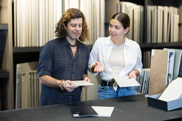 middle-aged couple in large hardware store chooses ceramic tiles and utensils for repair work in kitchen and bathroom.