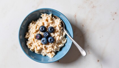 Top view oat bran porridge bowl with fresh blueberries and spoon on light marble background healthy breakfast flat lay concept