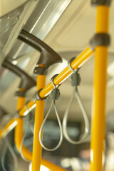 Empty urban bus straps and poles at dusk, yellow rails and hanging loops create repeating geometry, soft reflections on metal, calm offpeak atmosphere suggesting late shift cleaning or solitary