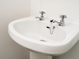 A white British style sink with two separate faucets and a drain. The sink is in a bathroom.