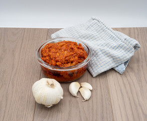 Indian garlic pickle and fresh garlic on a wooden table with a white background and blue kitchen towel