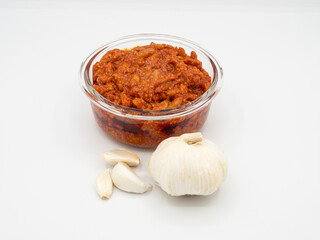 Indian garlic pickle in a bowl with fresh whole garlic on a white background