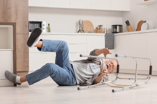 Senior man with walker falling on floor in kitchen