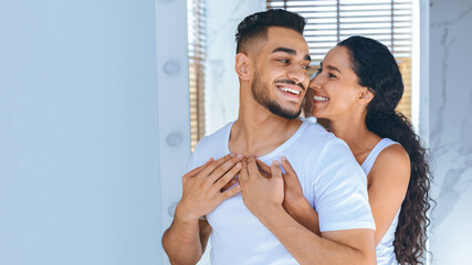 A young couple stands close in a warmly lit room, sharing smiles and laughter. They engage in a...