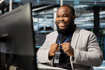 Smiling system administrator in data center checking infrastructure health report showing stable performance indicators. Joyful server room specialist euphoric after successfully completing operations