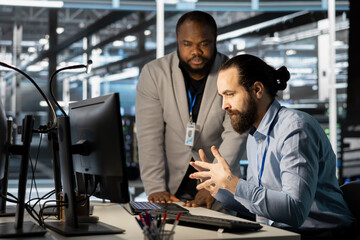 Technicians in data center office using computer, verifying firewall configurations. Teamworking IT specialists performing equipment vulnerability scans in server hub using PC